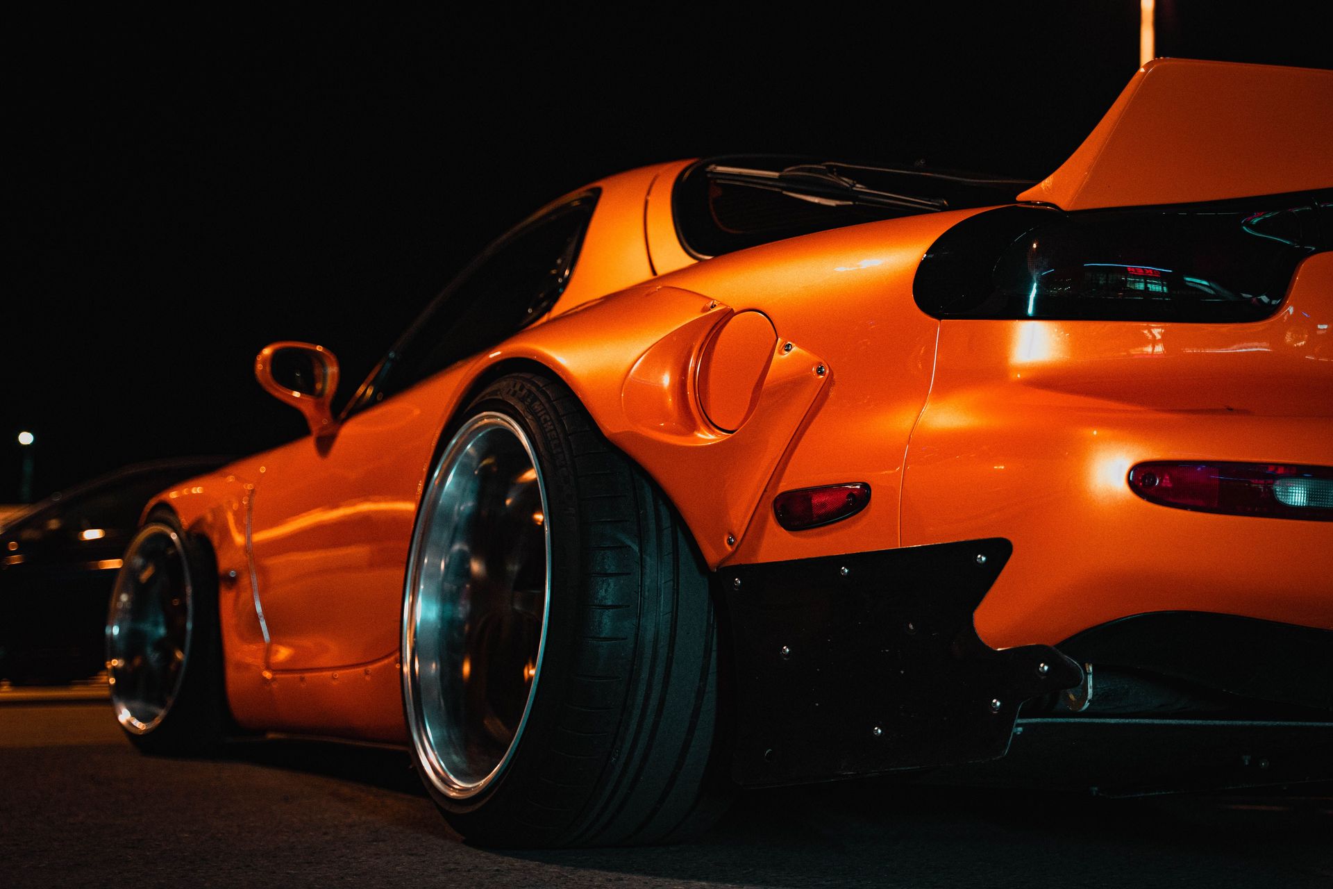Dynamic close-up of an orange sports car with custom modifications, captured at night.