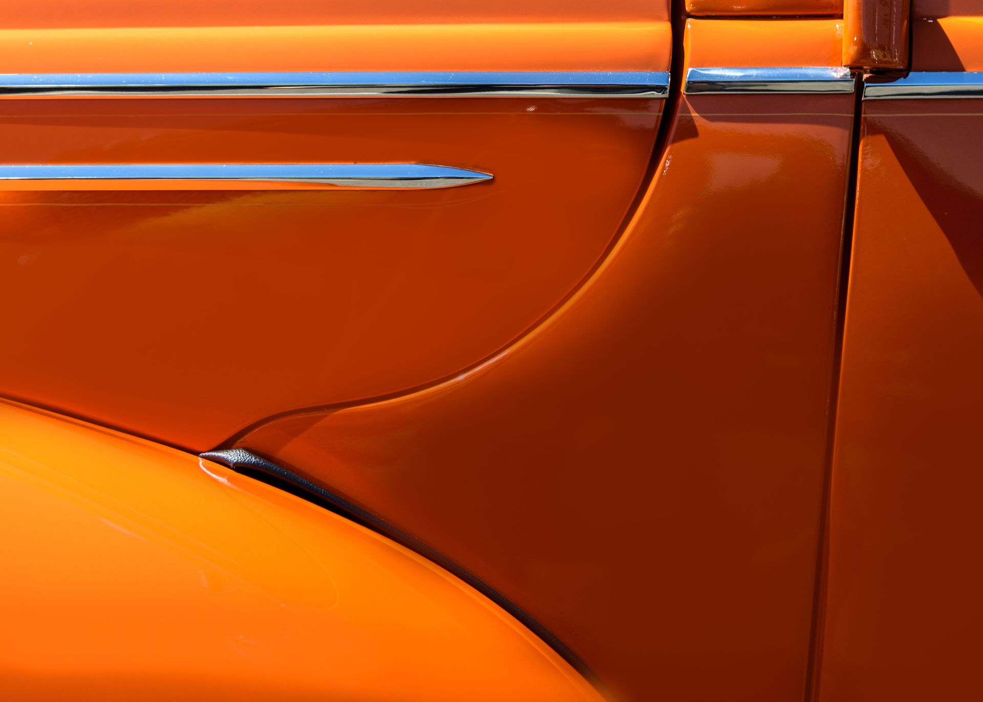Detailed close-up of a shiny orange vintage car with chrome accents.