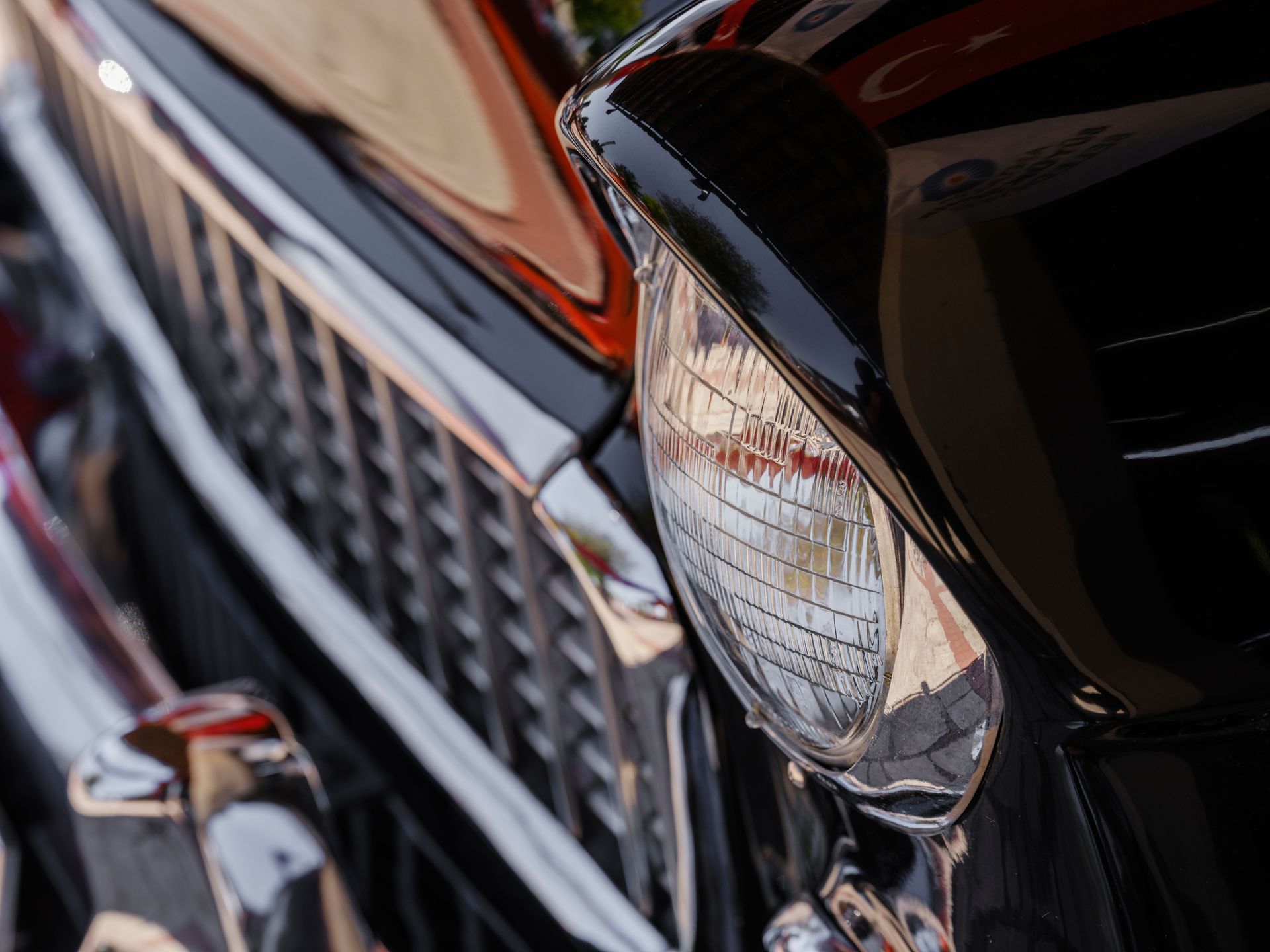 Detailed close-up of a vintage car's shiny headlight and grille, reflecting its classic design.